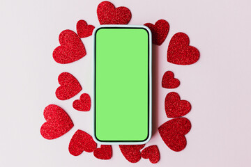 Happy Valentine's day digital mockup. Blank phone screen with space for text and stylish pink and red hearts flat lay on pink paper background. Smartphone love template