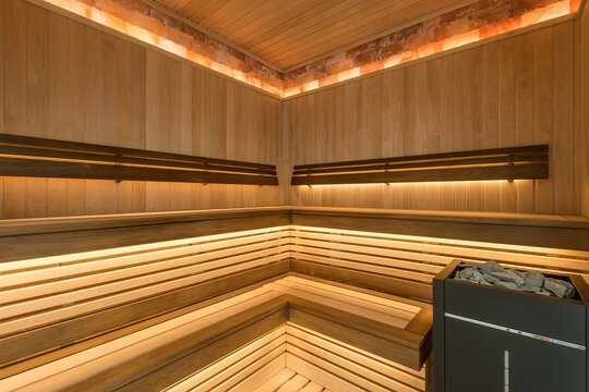 Sauna interior with benches made of light wood. Heating element with stones. Soft lighting.
