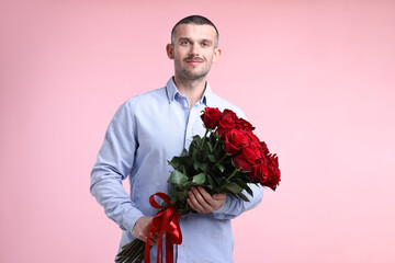 Valentine's day celebration. Man with beautiful bouquet of red roses on pink background