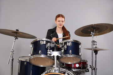 Teenage girl with drumsticks and drums on light grey background