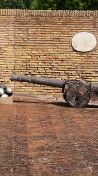 aged cannons wooden carriages flank stacked pyramid stone cannonballs artillery display sits against weathered brick fortification wall historic castel sant'angelo rome italy heavy 