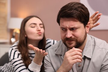 Naklejka premium Embarrassed man refusing kiss from young woman at home, selective focus