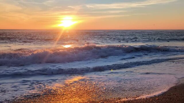 Bright golden sunrise sun shining on horizon with waves hitting sand sea shore 