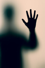 Mysterious silhouette pressing hand against frosted glass.