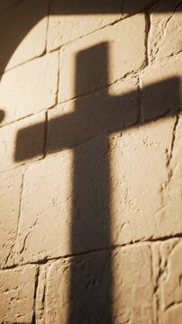 Cross shadow cast on stone wall in chapel. Light from window creates spiritual scene. Concept of religion, faith, worship. Symbolic presence in spiritual places