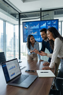 Three diverse colleagues discuss business analytics in modern office with large screen displaying charts and graphs. Teamwork, data analysis, and digital marketing concepts are highlighted.