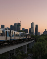 Urban metro train crossing elevated track with modern city skyline at sunset