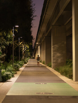 man jogging on illuminated urban pathway at night under elevated structure
