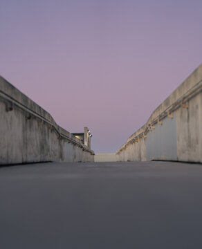 Minimal concrete walkway with symmetrical walls under pastel sky