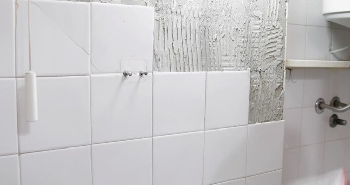 Construction worker demolishing and removing ceramic tiles in bathroom wearing protective gloves, close up