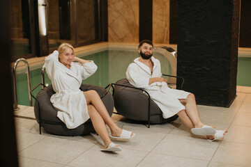 Couple relaxing poolside in bathrobes at resort spa