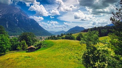 Fototapeta premium Peaceful picturesque mesmerizing atmospheric landscape with wild alpine meadow grasslands pasture, and mountains on summer day with blus sky and clouds
