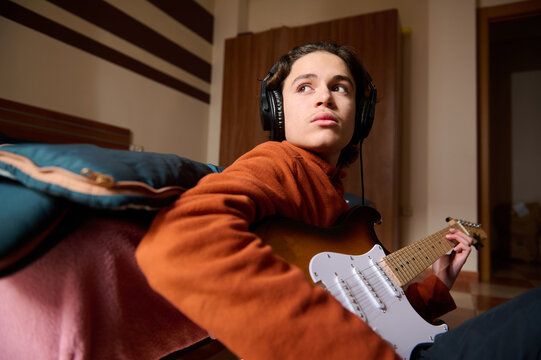 Teenager Playing Electric Guitar With Headphones On Couch In Cozy Room