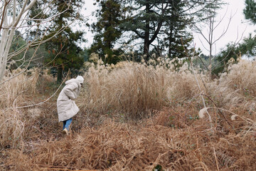 Person in coat stands amid tall dry grass in a winter field, capturing a solitary outdoor moment in...