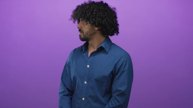 Man with curly hair and visible face wearing blue shirt turns head to left against purple backdrop in studio; contemplative solitude.