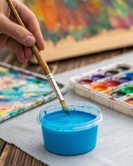 Fototapeta premium Artistic expression closeup of a hand dipping a brush into vivid blue acrylic paint on a messy palette in a boho environment