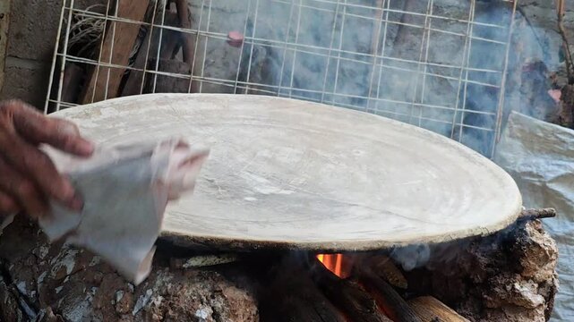 Person cleaning a clay comal surface with lime water, traditional preparation before baking.