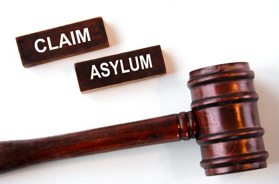 CLAIM ASYLUM - words on wooden brown bars on a white background with a judge's gavel