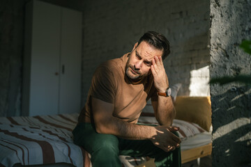Obraz premium Man experiencing headache and stress sitting in bedroom