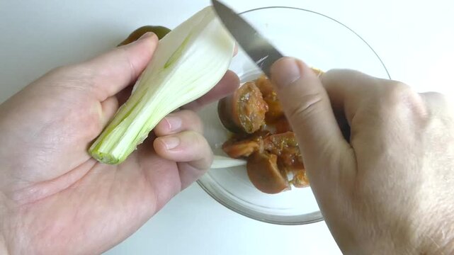 Person preparing spring onion for salad on white background