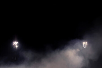 Fototapeta premium Two stadium floodlight arrays glowing through dense fog at night, symmetrical composition with smoke and mist