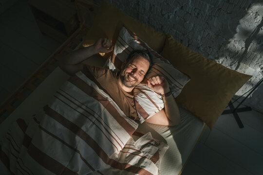 Man waking up in bed rubbing eyes from morning sunlight