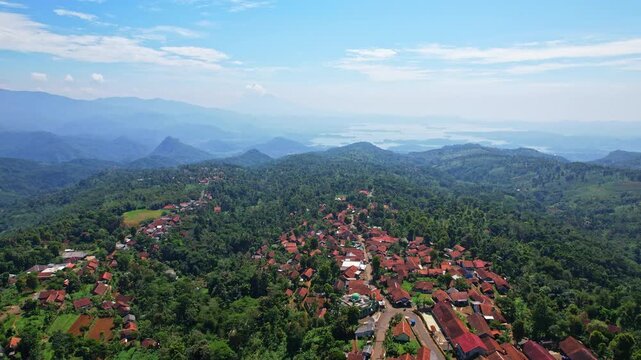 Aerial drone footage of a wide green valley with forests around, Sukajadi village in the front, in Sumedang regency, Java island, Indonesia, with Jatigede water reservoir behind, and wide mountains