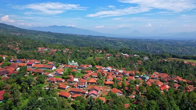 Aerial drone footage of Sukajadi village in the front, in Sumedang regency, Java island, Indonesia, with wide green valley with forests around, and wide mountains, and a mosque in the center