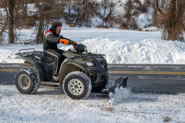 Senior man in fur hat and snowsuit plows huge snow with off-road vehicle all-terrain ATV,  side view plowed street and rural snowy landscape background with copy space