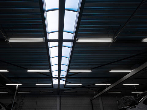 Industrial warehouse ceiling with long skylight and fluorescent tube lights, dark corrugated metal roof