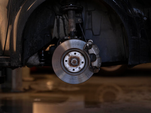 Car brake disc and caliper visible with wheel removed, automotive workshop repair and maintenance scene
