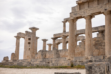 Fototapeta premium Ancient Greek temple ruins with massive stone columns standing against a cloudy sky. Weathered Doric columns and broken stone blocks reveal the architectural strength and timeless beauty 
