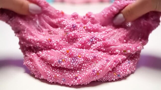 Sensory pink slime with foam beads being stretched and pulled, satisfying and colorful close up