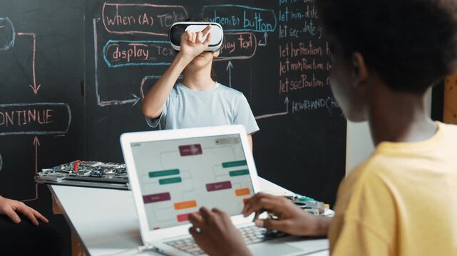 African boy programming system while caucasian girl enter metaverse while sitting at blackboard with engineering code written.high school girl wearing VR or headset in STEM technology. Edification