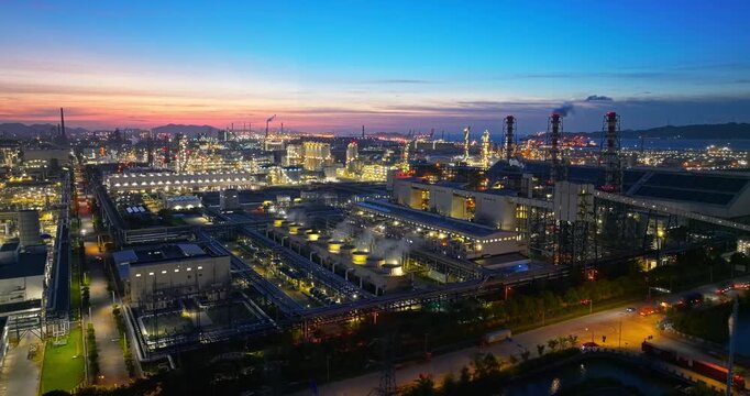 Aerial shot of a massive industrial chemical plant and oil refinery complex at dusk with glowing lights.