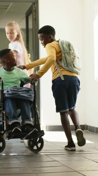 Vertical video: Holding door, yellow helper helping friend in wheelchair into school hall with pack