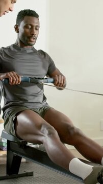 Vertical video: Rowing man inhaling for form, driving legs pulling on rower at home grey tee watch