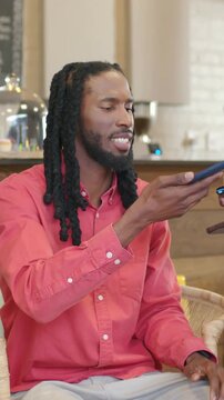 Vertical video: Showing phone to friend, dreadlocked man in coral shirt tapping blue phone at cafe
