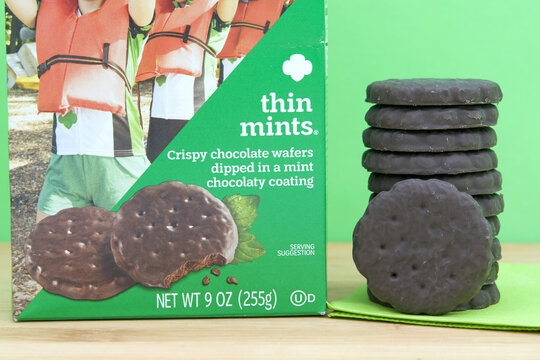 Alameda, CA - Jan 27, 2026: One box of ABC Baker brand Girl Scout cookies, Thin Mints on light wood table, stack of cookies on green napkin. Green background