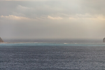 Fototapeta premium 日の出の海。 ぐんじ山展望台から見る美しい伊豆諸島の海。 沖には新島や神津島が見える。 白い石灰岩の崖、白ママ断崖の沖には無人島の早島。 乗用車を乗せた大型貨物船や漁船も見える。 式根島は東京都心から南へ160km。 外周12kmの小さな有人島。 温かい黒潮が当たり水温と水質が高い。 また、リアス式の入り組んだ入り江が多く、海水浴や釣りが盛ん。 温泉島としても有名。海際に多くの無料露天風呂がある。