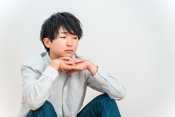 A young Asian man resting his chin on his hand and looking down blankly © buritora