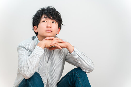 A young Asian man resting his chin on his hand and staring blankly into the distance