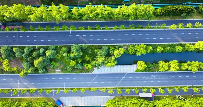 Aerial shot of parallel asphalt roads with green trees and a blue canal in a modern city during the day.