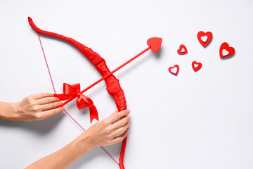 Naklejka premium Female hands with red cupid's bow and hearts on light background. Valentine's Day celebration