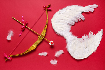 Naklejka premium Composition with cupid's bow, wings and feathers on red background. Valentine's Day celebration