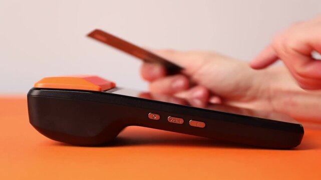 Woman with credit card using payment terminal at orange table, closeup