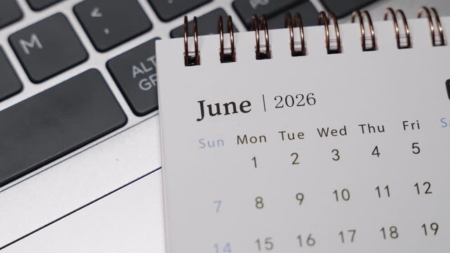 Close-up of a desk calendar showing June 2026 placed next to a laptop keyboard. Camera slowly rotates to the right, revealing clear date layout and calm monthly planning concept in a modern workspace.