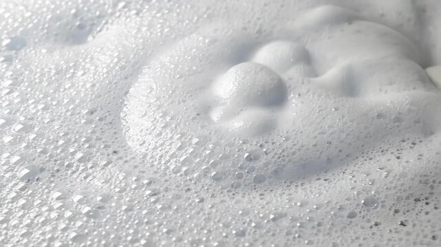Close up of a hand moving through white soap foam bubbles showing detailed texture and airy lightness