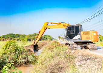 The heavy machinery is surrounded by green vegetation and fields under a clear blue sky.