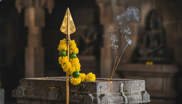 Golden spear decorated with marigold flowers and burning incense on a stone altar in an ancient Hindu temple for traditional worship concept
